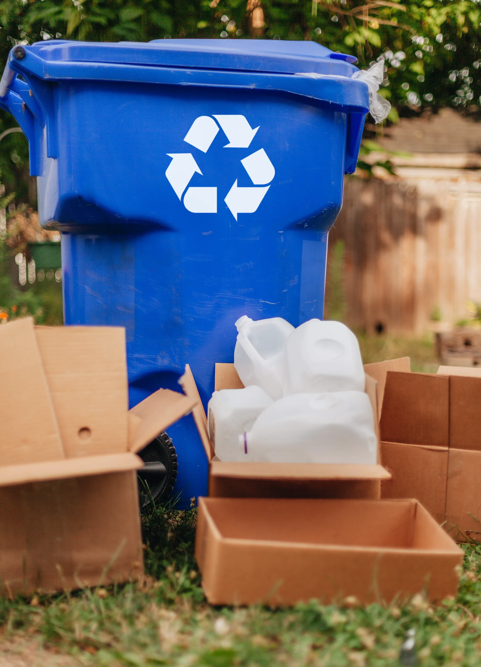 Blaue Mülltonne für Recycling mit Kartons im Vordergrund