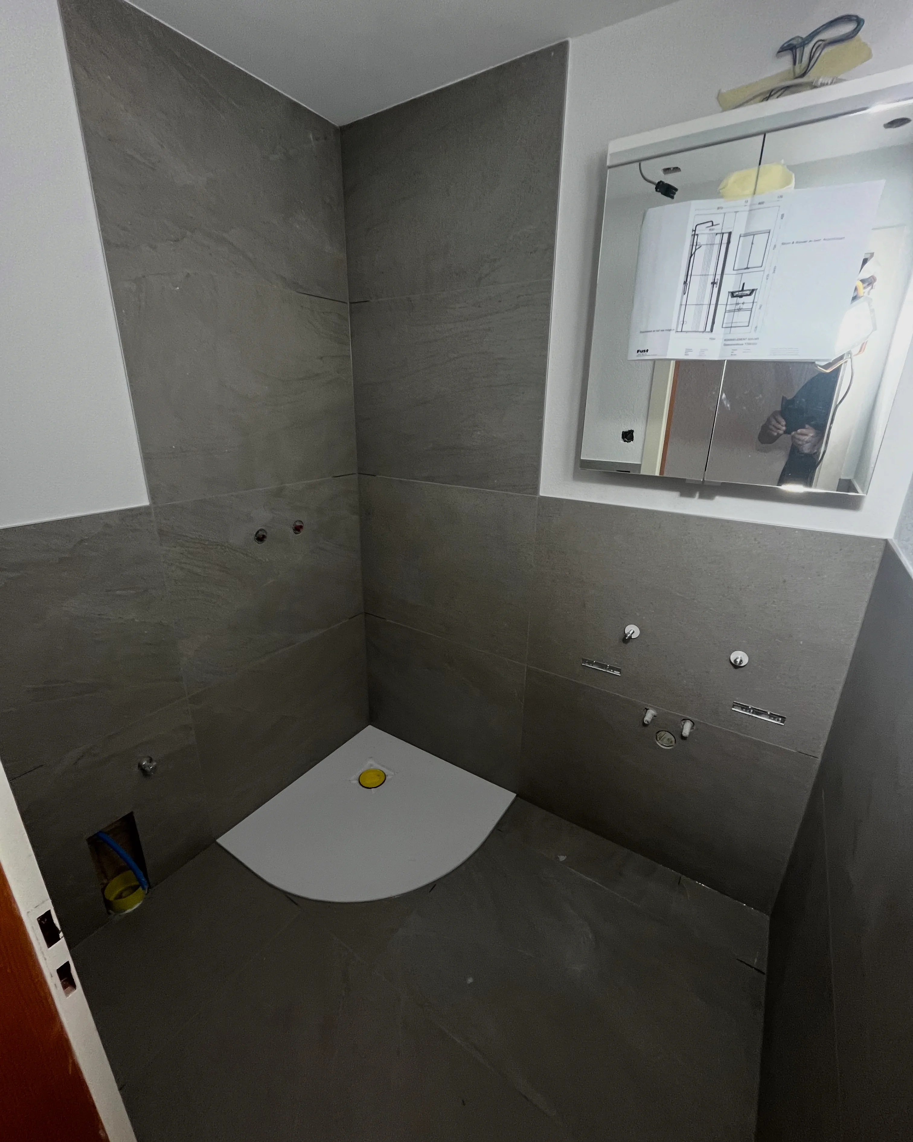 Badezimmer mit grauen Wand- und Bodenplatten, vorbereitet für die Installation von Sanitäranlagen