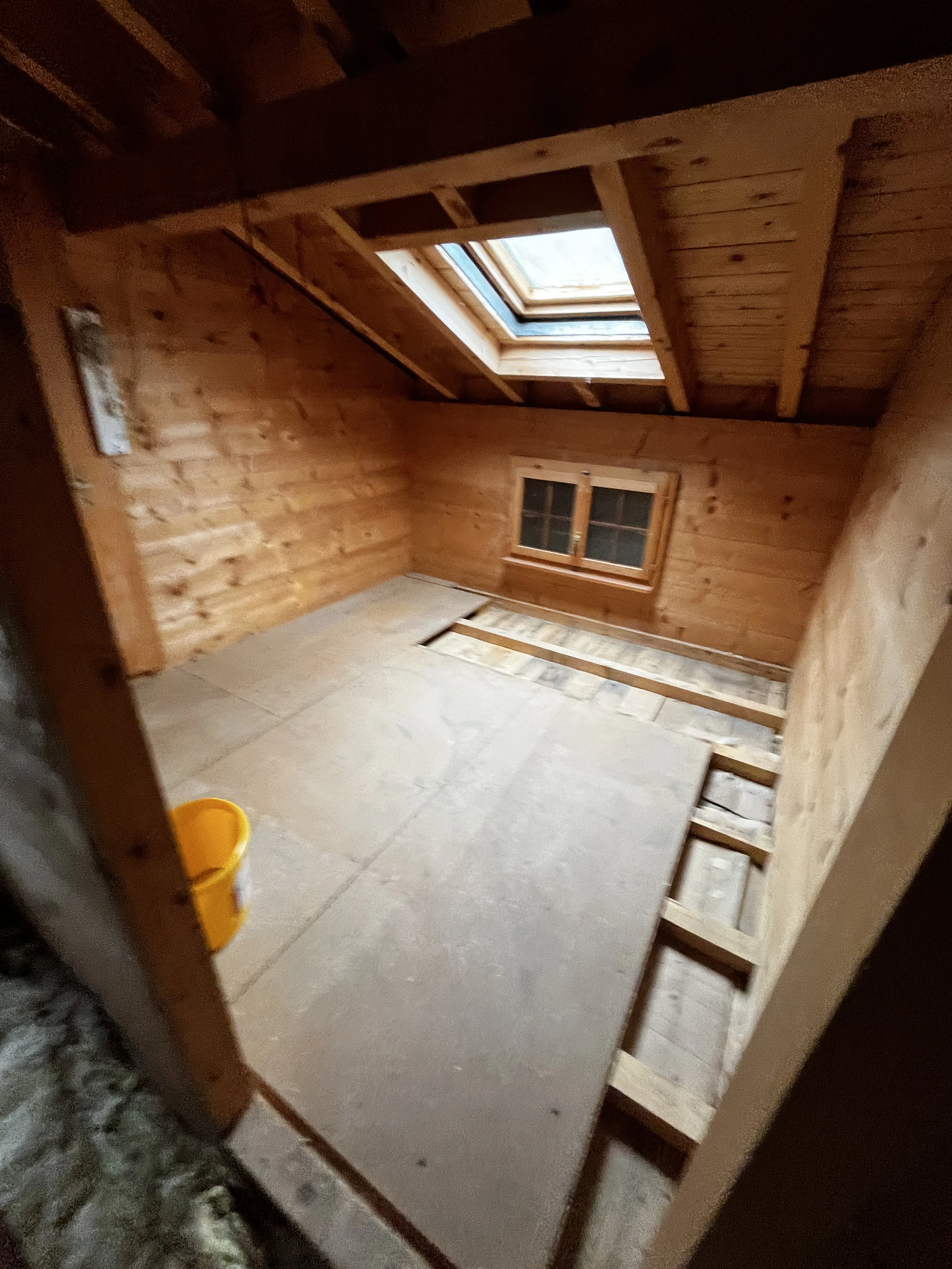 Leere Holzstube mit Holzdecke und Dachfenster, bereit für Bodenverlegung