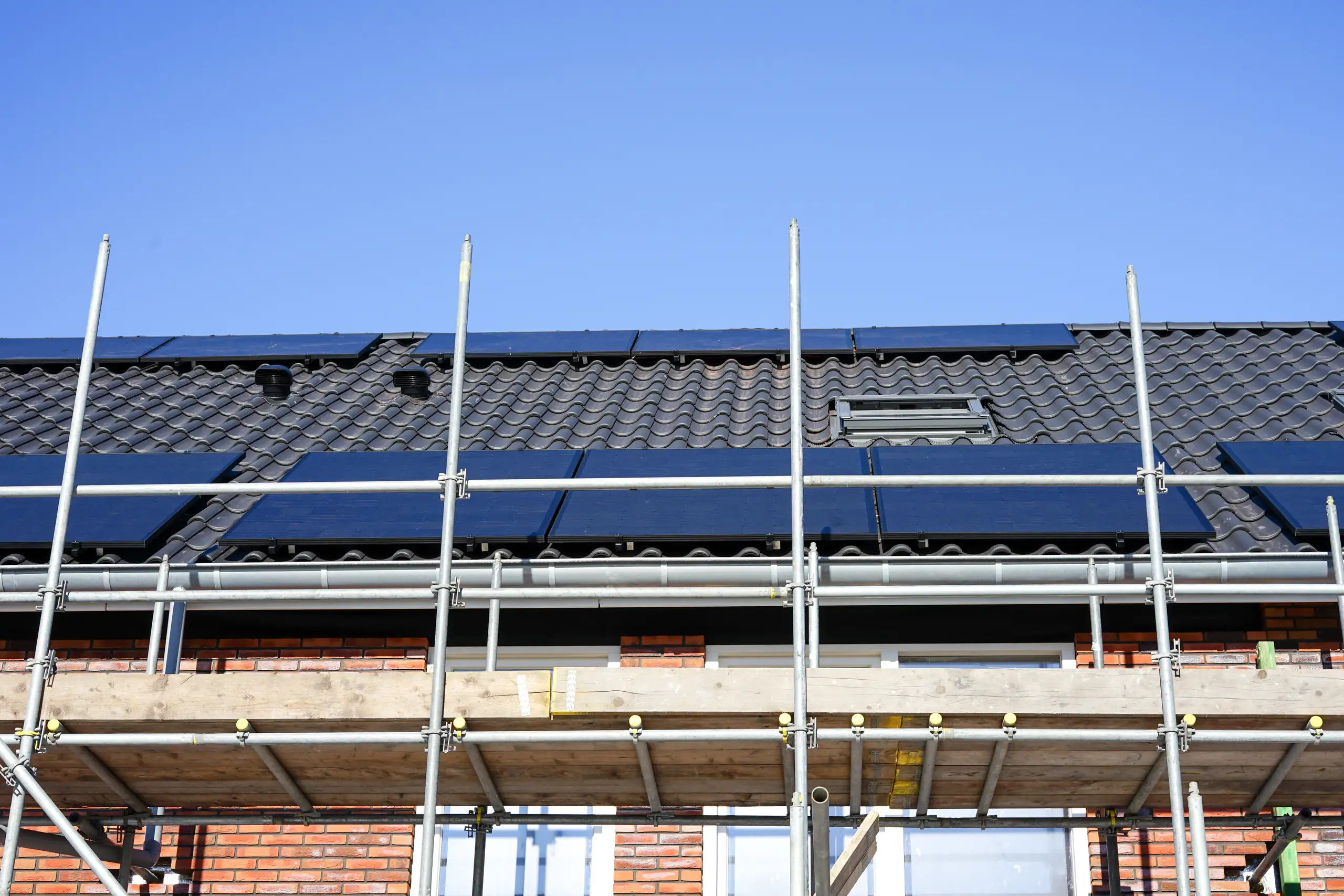 Fassade eines Gebäudes mit Gerüst und Solarpanelen auf dem Dach