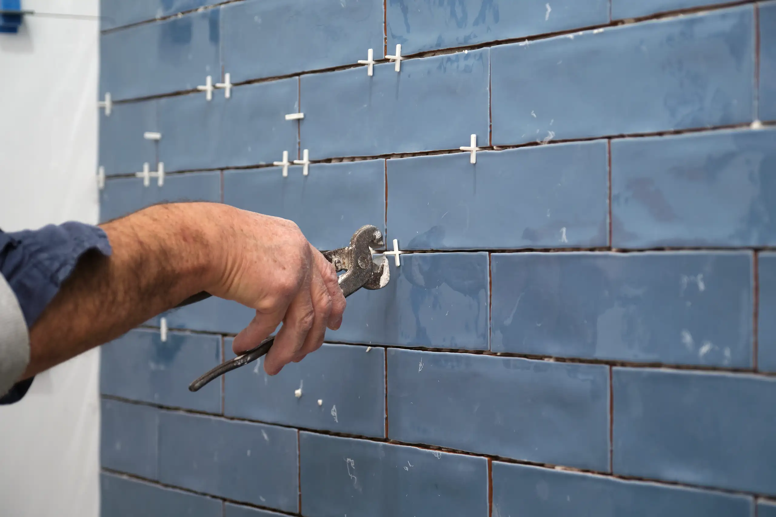 Handwerker verlegt blaue Wandfliesen mit Zange, präzise Ausführung