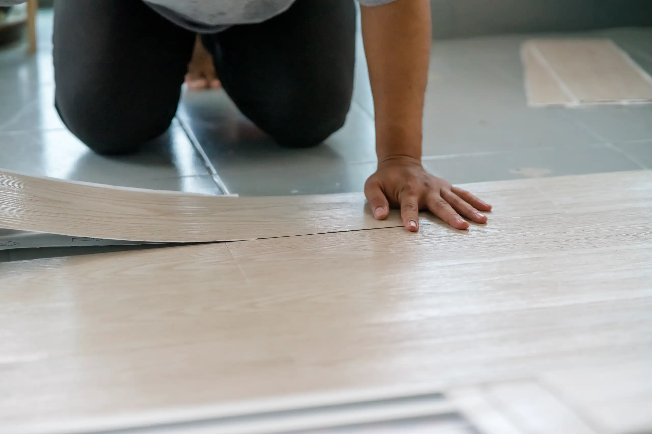 Eine Person verlegt Vinylboden auf einer Fläche, konzentriert am Arbeiten